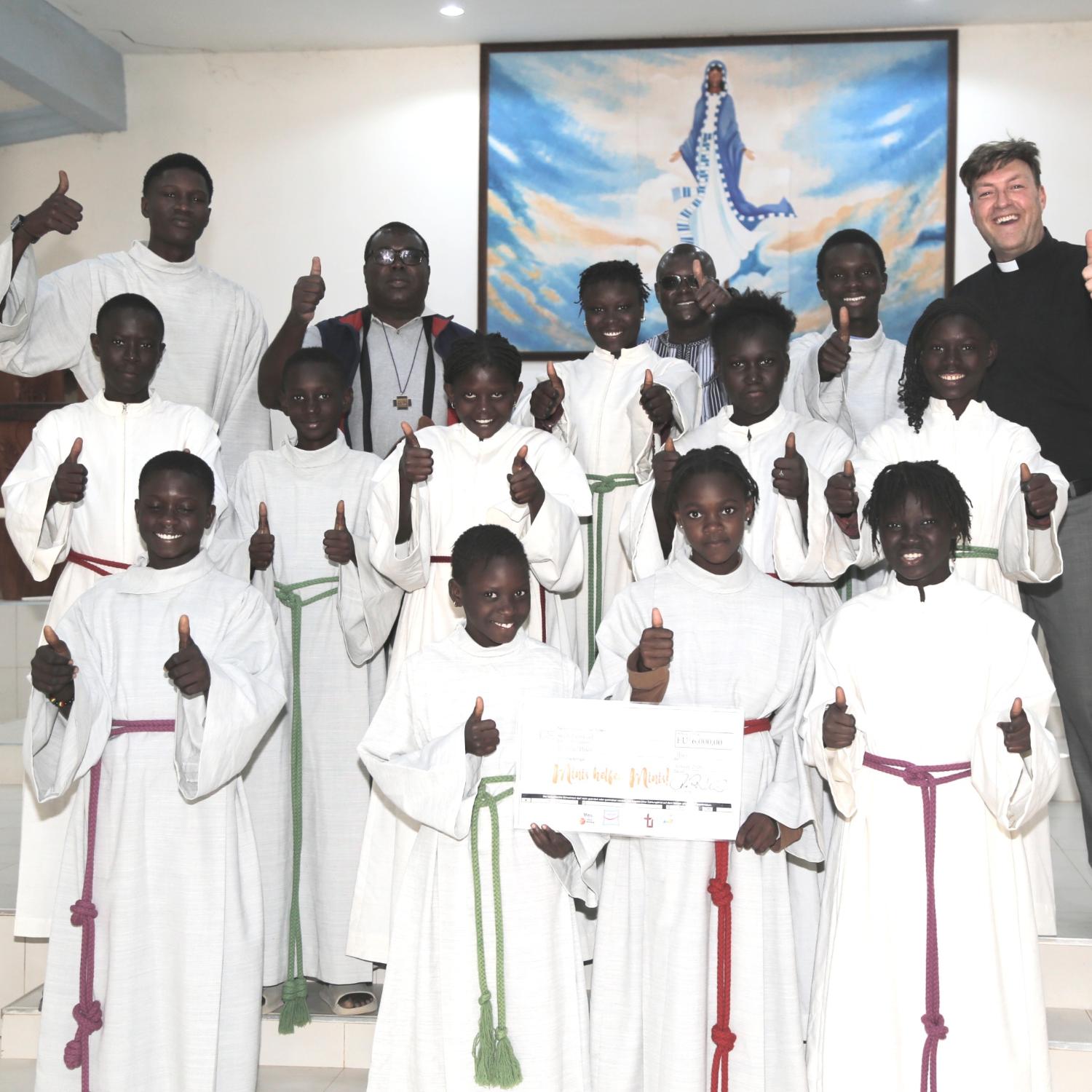 Freuen sich über den Erfolg der Aktion „Minis helfen Minis“: Diözesanjugendpfarrer Gerd Richard Neumeier (oben rechts), sein Kollege Abbé Etienne Mbengue (oben, zweiter von links) und die Ministrant*innen aus Mont Rolland mit den aus der Erzdiözese Bamberg gespendeten Minigewändern.